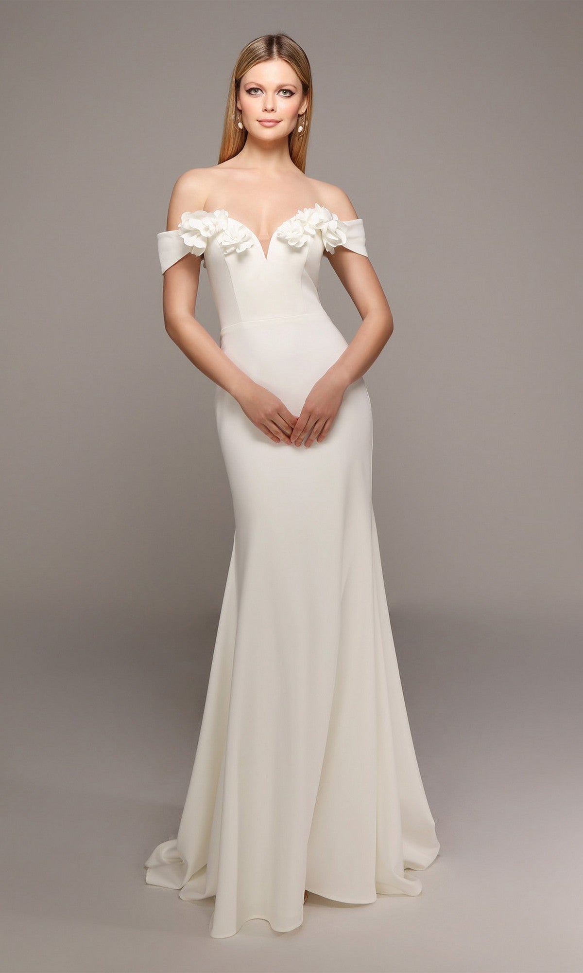 A woman poses against a neutral background in the Alyce 7062 long formal dress—an off-the-shoulder, fitted white gown with 3D floral accents on the neckline.